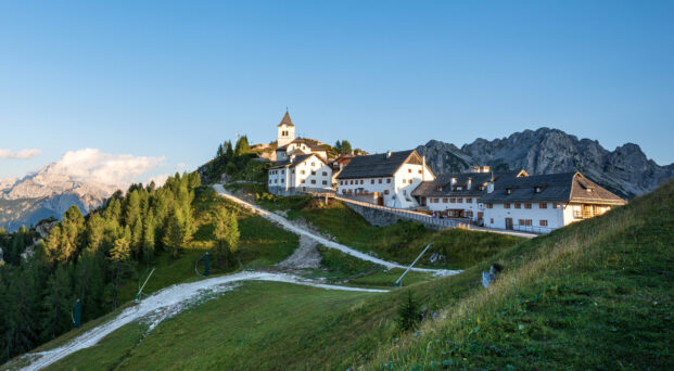 Small and ancient village of Lussari or Monte Santo di Lussari (1790 m) and the peak of Mangart mountain (2677 m.). Julian Alps, Tarvisio, Udine province, Friuli Venezia Giulia, Italy, Europe.